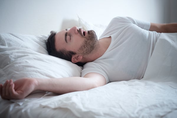 Man sover med öppen mun i säng