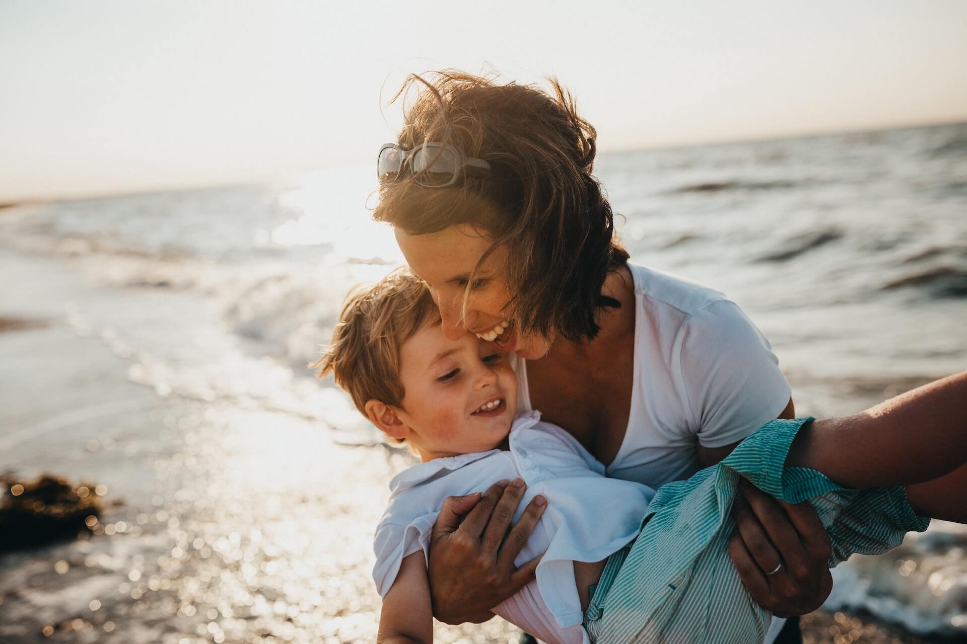 Mom carries a child and laughs on the beach